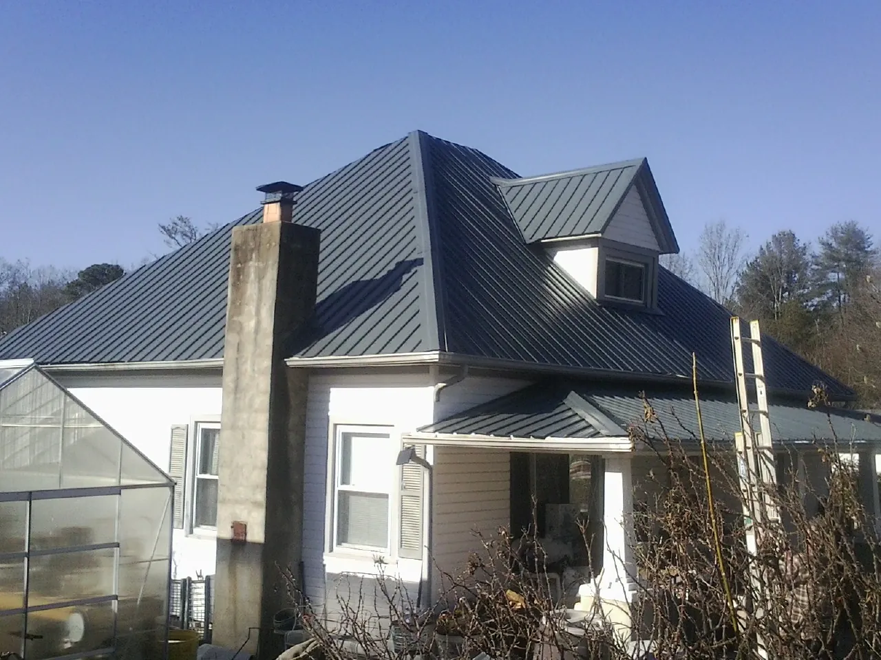 Dark blue standing seam metal roof on a white farmhouse with dormer — Slate & Tile Roof Repair by Roofing Brothers in Halstead