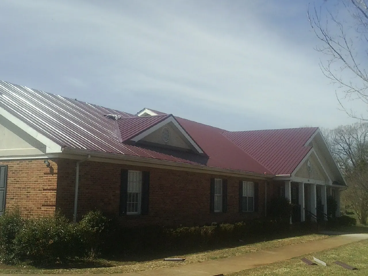 Red metal roof with gabled entries on a long brick building, from a Hail Damage Roof Repair job in Halstead