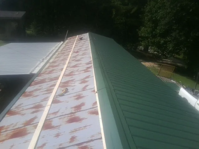 Old rusted panels beside newly installed green metal roofing — Wind Damage Roof Repair by Roofing Brothers in Halstead