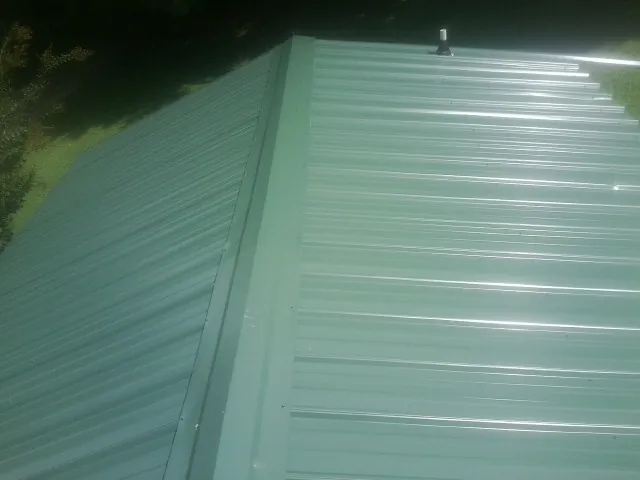 New green metal panels meeting at the ridge of a roof — Flat Roof Repair work by our crew in Halstead