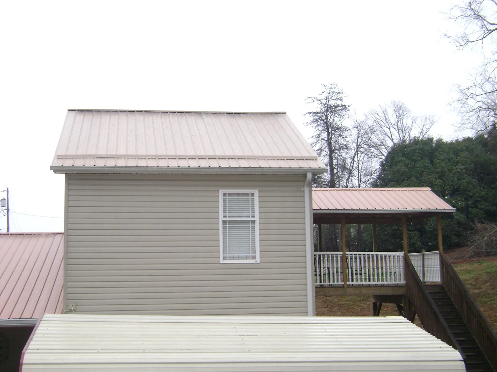 Tan metal roofs on a two story addition and attached porch, from a Roof Replacement job in Halstead